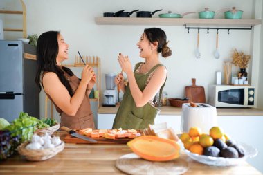Birlikte müzik eşliğinde dans eden mutlu Asyalı kızlar mutfakta yemek yapmaktan zevk alıyorlar. İki kadın kahvaltı hazırlarken eğleniyor. Asyalı bayan arkadaşlar evde mikrofon olarak spatula ile şarkı söylüyorlar..