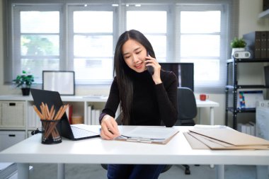 Tutkulu insanlar bir şeyleri gerçekleştirir. Modern bir ofisteki masasında cep telefonu kullanan Asyalı genç bir iş kadınının fotoğrafı..