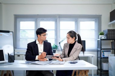 İş kadını ve işadamı mali tabloları analiz ediyor ve masa başında iş stratejilerini tartışıyor, kalemleri tutuyor ve basılı belgeleri birlikte inceliyor..