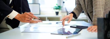 İş kadını ve işadamı mali tabloları analiz ediyor ve masa başında iş stratejilerini tartışıyor, kalemleri tutuyor ve basılı belgeleri birlikte inceliyor..