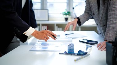 İş kadını ve işadamı mali tabloları analiz ediyor ve masa başında iş stratejilerini tartışıyor, kalemleri tutuyor ve basılı belgeleri birlikte inceliyor..