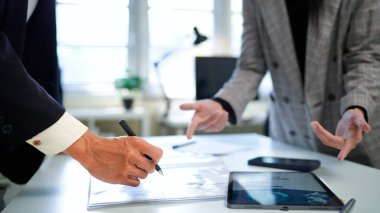 İş kadını ve işadamı mali tabloları analiz ediyor ve masa başında iş stratejilerini tartışıyor, kalemleri tutuyor ve basılı belgeleri birlikte inceliyor..