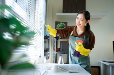 Genç Asyalı kadın, üniformalı hademe kadın antiseptik sprey şişesi ve ıslak bez temizleme masaüstü bilgisayarı, masa ve masa yüzeyleri modern ofis odasının içinde..