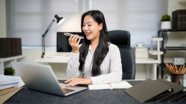 İş kadını, ofisteki akıllı telefonuyla ses asistanıyla iletişim kurarak yapay zeka kullanımını öneriyor..