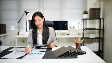 Bitmemiş belgeyi aramak ve kontrol etmek için tablet kâğıt dosyaları üzerinde çalışan iş kadını, yoğun çalışma masasındaki klasörlerdeki belgelerde başarıya ulaştı.