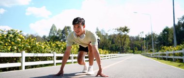 Gülümseyen aktif adam başlangıç pozisyonunda oturuyor, koşuyor, yürüyor parkta spor yapıyor..