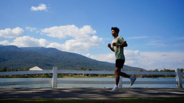 Yolda koşan genç bir adamın silueti. Açık havada peyzaj ve gökyüzü arkaplanlı spor yaparken formda bir fitness koşucusu.