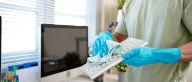 Person cleaning room, cleaning worker is using cloth to wipe computer keyboard in company office room. Cleaning staff. Concept of cleanliness in the organization.