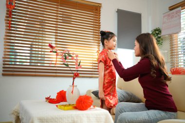 Ulusal kostümlü gülümseyen Asyalı küçük kız Çin Yeni Yılı kırmızı zarf paketi alıyor. Evdeki kanepede oturan annesinden. Mutlu Çin Yeni Yıl aile kavramı..