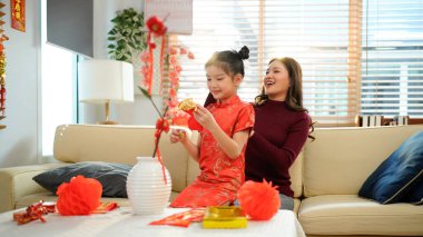 Ulusal kostümlü gülümseyen Asyalı küçük kız Çin Yeni Yılı kırmızı zarf paketi alıyor. Evdeki kanepede oturan annesinden. Mutlu Çin Yeni Yıl aile kavramı..