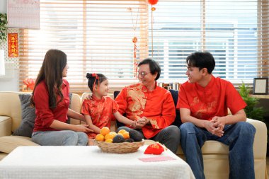 Mutlu Asyalı aile, Çin Yeni Yılı 'nı kutlamak için evde toplanıyor, kanepede oturuyor, konuşuyor, kırmızı zarf veriyor ve yemek yiyor..