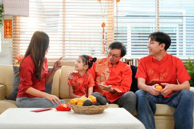 Mutlu Asyalı aile, Çin Yeni Yılı 'nı kutlamak için evde toplanıyor, kanepede oturuyor, konuşuyor, kırmızı zarf veriyor ve yemek yiyor..