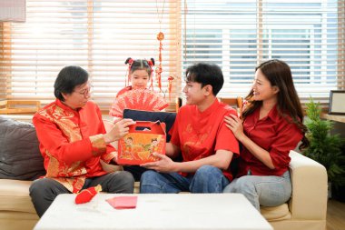 Asyalı küçük kız, annesi ve babası bahar festivalinde hediye kutusuyla dedesini ziyaret ederken mutlu yaşlı bir adam torununun omuzlarını okşuyor ve onu övüyordu..