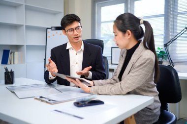 İş kadını ve işadamı mali tabloları analiz ediyor ve masa başında iş stratejilerini tartışıyor, kalemleri tutuyor ve basılı belgeleri birlikte inceliyor..