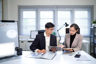 İş kadını ve işadamı mali tabloları analiz ediyor ve masa başında iş stratejilerini tartışıyor, kalemleri tutuyor ve basılı belgeleri birlikte inceliyor..