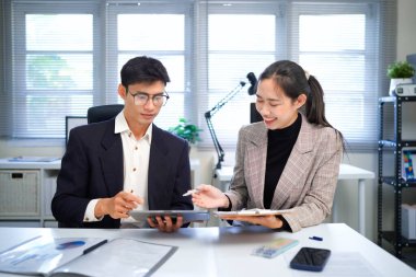 İş kadını ve işadamı mali tabloları analiz ediyor ve masa başında iş stratejilerini tartışıyor, kalemleri tutuyor ve basılı belgeleri birlikte inceliyor..