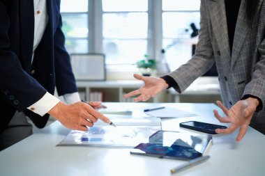 İş kadını ve işadamı mali tabloları analiz ediyor ve masa başında iş stratejilerini tartışıyor, kalemleri tutuyor ve basılı belgeleri birlikte inceliyor..