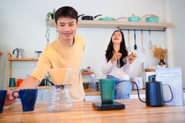 Birkaç Asyalı ya da bir çift kahve çekirdeğini öğütmeye, mutfakta kahve yapmaya ya da demlemeye. Bardak, kupa, şişe ve mutfak malzemelerini de masaya koyun. Sabah yaşam tarzı kavramı, aşk, mutluluk, aile, ilişki..