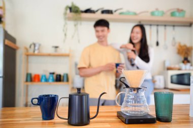 Birkaç Asyalı ya da bir çift kahve çekirdeğini öğütmeye, mutfakta kahve yapmaya ya da demlemeye. Bardak, kupa, şişe ve mutfak malzemelerini de masaya koyun. Sabah yaşam tarzı kavramı, aşk, mutluluk, aile, ilişki..