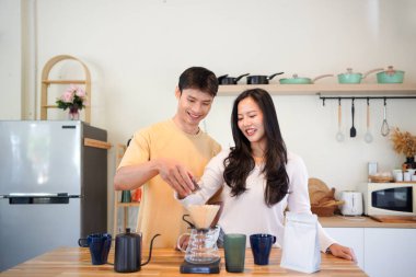 Genç aşık çift, modern mutfakta kahve damlatıcısının üzerinde kahve yaparken hafta sonu sabahlarını birlikte geçiriyorlar..