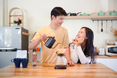 Genç aşık çift, modern mutfakta kahve damlatıcısının üzerinde kahve yaparken hafta sonu sabahlarını birlikte geçiriyorlar..