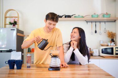 Genç aşık çift, modern mutfakta kahve damlatıcısının üzerinde kahve yaparken hafta sonu sabahlarını birlikte geçiriyorlar..