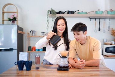 Genç aşık çift, modern mutfakta kahve damlatıcısının üzerinde kahve yaparken hafta sonu sabahlarını birlikte geçiriyorlar..