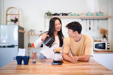 Genç aşık çift, modern mutfakta kahve damlatıcısının üzerinde kahve yaparken hafta sonu sabahlarını birlikte geçiriyorlar..