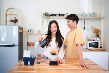 Genç aşık çift, modern mutfakta kahve damlatıcısının üzerinde kahve yaparken hafta sonu sabahlarını birlikte geçiriyorlar..