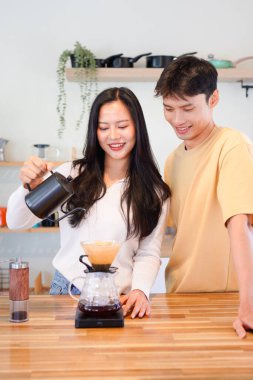 Genç aşık çift, modern mutfakta kahve damlatıcısının üzerinde kahve yaparken hafta sonu sabahlarını birlikte geçiriyorlar..