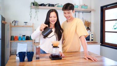 Genç aşık çift, modern mutfakta kahve damlatıcısının üzerinde kahve yaparken hafta sonu sabahlarını birlikte geçiriyorlar..