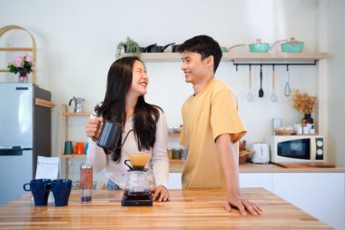 Genç aşık çift, modern mutfakta kahve damlatıcısının üzerinde kahve yaparken hafta sonu sabahlarını birlikte geçiriyorlar..