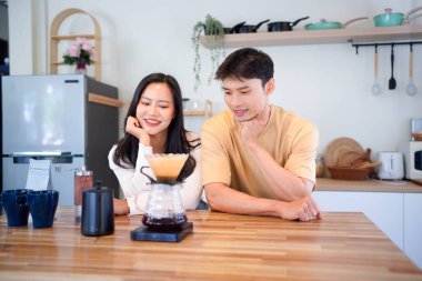 Genç aşık çift, modern mutfakta kahve damlatıcısının üzerinde kahve yaparken hafta sonu sabahlarını birlikte geçiriyorlar..