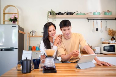 Modern mutfakta dijital tablet kullanan mutlu çift, kahvaltı veya kahveden ve internet içeriğinden keyif alıyor.