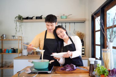 Yatay mutlu çift sıcacık bir ev mutfağında makarna pişiriyor sıcak ışık, tencere ve doğal renklerden yükselen buhar neşeli ve samimi bir atmosfer yaratıyor, yaşam tarzı için ideal..