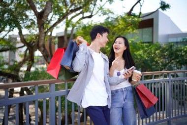 Güzel, genç bir çift alışverişte eğleniyor, cep telefonuyla eğleniyor, alışveriş yaptıktan sonra parkta duran güzel, gülümseyen genç bir çiftin portresi..