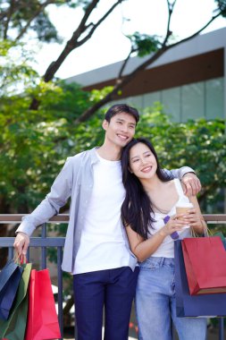 Alışveriş torbalarıyla mutlu bir çift alışveriş merkezinin önünde kahve molası veriyor, mutlu anlarını paylaşıyorlar..