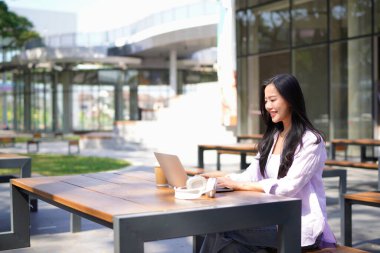 Dizüstü bilgisayarı olan, şık giysili genç ve güzel bir kadın ofis binasının önünde oturmuş internetten ders çalışıyor. Bilgisayarda internet üzerinden ticaret dersi dinleyen yetişkin bir öğrenci.