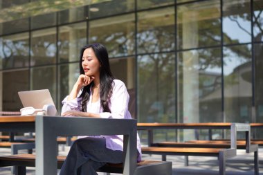 Dizüstü bilgisayarı olan, şık giysili genç ve güzel bir kadın ofis binasının önünde oturmuş internetten ders çalışıyor. Bilgisayarda internet üzerinden ticaret dersi dinleyen yetişkin bir öğrenci.