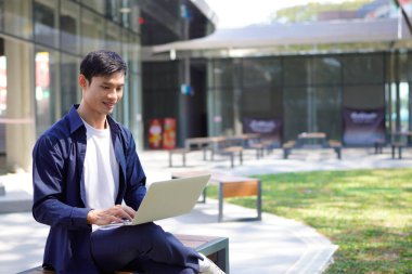 Modern şehir ortamında bankta oturan yakışıklı Asyalı iş adamı ya da dizüstü bilgisayarda yazan öğrenci..