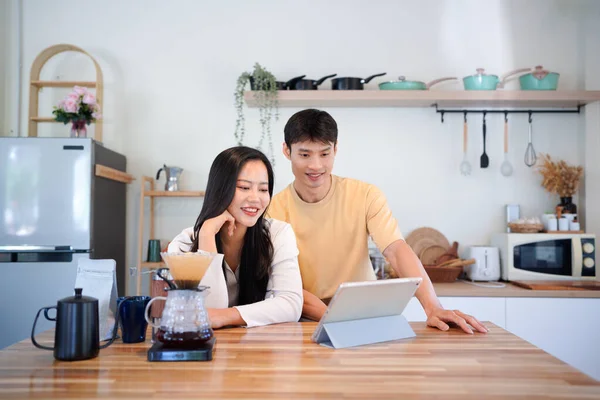 Modern mutfakta dijital tablet kullanan mutlu çift, kahvaltı veya kahveden ve internet içeriğinden keyif alıyor.