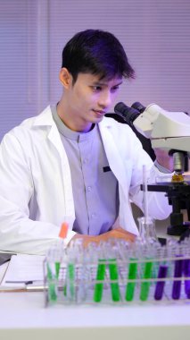 Laboratuvar ortamında deney tüpleri ve deney tüpleriyle çalışan laboratuvar önlüklü Asyalı erkek bilim adamı. Mikroskop ve araştırma ve deney ile bilgisayar..