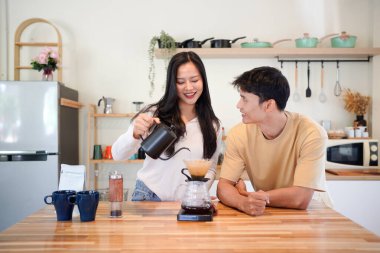 Genç aşık çift, modern mutfakta kahve damlatıcısının üzerinde kahve yaparken hafta sonu sabahlarını birlikte geçiriyorlar..