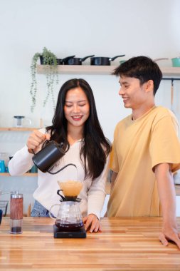 Genç aşık çift, modern mutfakta kahve damlatıcısının üzerinde kahve yaparken hafta sonu sabahlarını birlikte geçiriyorlar..