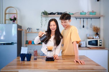 Genç aşık çift, modern mutfakta kahve damlatıcısının üzerinde kahve yaparken hafta sonu sabahlarını birlikte geçiriyorlar..