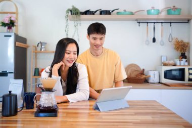 Modern mutfakta dijital tablet kullanan mutlu çift, kahvaltı veya kahveden ve internet içeriğinden keyif alıyor.