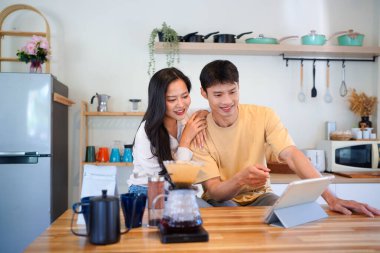 Modern mutfakta dijital tablet kullanan mutlu çift, kahvaltı veya kahveden ve internet içeriğinden keyif alıyor.