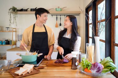 Yatay mutlu çift sıcacık bir ev mutfağında makarna pişiriyor sıcak ışık, tencere ve doğal renklerden yükselen buhar neşeli ve samimi bir atmosfer yaratıyor, yaşam tarzı için ideal..