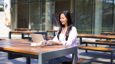 Dizüstü bilgisayarı olan, şık giysili genç ve güzel bir kadın ofis binasının önünde oturmuş internetten ders çalışıyor. Bilgisayarda internet üzerinden ticaret dersi dinleyen yetişkin bir öğrenci.