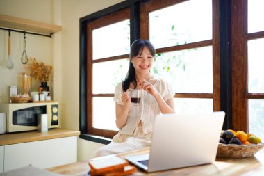Genç iş kadını uzaktan iş yönetiyor, dizüstü bilgisayar kullanıyor sabahları mutfak tezgahında oturuyor, kişisel gelişim üzerine çalışıyor..